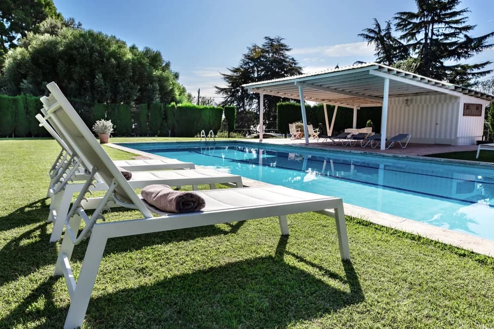 Sun loungers on the lawn beside the villa's outdoor pool, with a white pergola at the far end